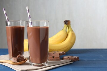 Tasty chocolate milk in glasses, pieces and bananas on blue wooden table, space for text
