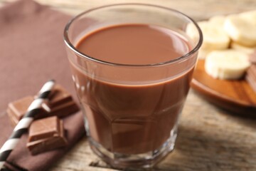 Tasty chocolate milk, pieces and banana on wooden table, closeup