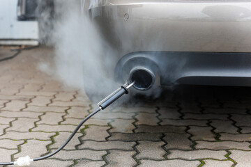 Car exhaust pipe emits dense smoke during emission test city pavement. Pollution control device...