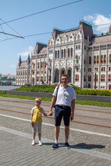 Obraz premium Summer Day Family Time: Dad and Son Visiting the Majestic Parliament Building, Hungary