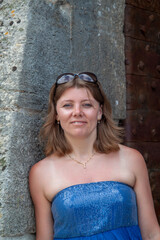 Blue dress for a formal event: portrait of a blond woman in a blue sparkling strapless dress posing near a stonewall