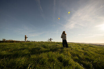 Fototapeta premium Father and daughters flying kites in a green meadow on windy day