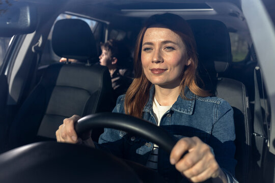 Happy young woman driving a car with a kid in the backseat