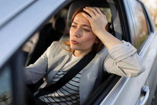 Woman sitting in a car holding her head while lost in toughts