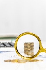 Magnifying glass reveals stacked coins on a financial document with a calculator in the background