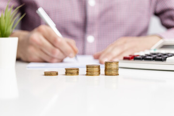 Person calculating finances with stacked coins and calculator at a desk during daytime