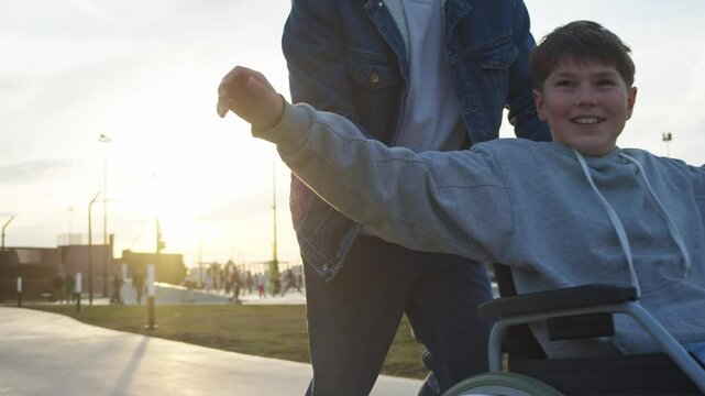 Father is driving his son, with special health needs and uses wheelchair, at fast pace. They are enjoying their time together in city park, which has accessible environment.