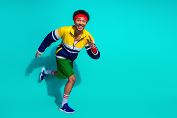 Energetic young man in retro fashion sportswear striking a dynamic pose against a teal background showing vitality and playfulness