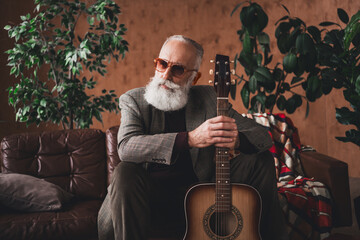 Stylish senior man in retro interior holding guitar surrounded by plants