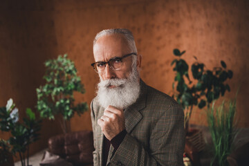 Portrait of senior gentleman in a vintage plaid suit with glasses and a white beard, surrounded by indoor greenery and warm retro interior