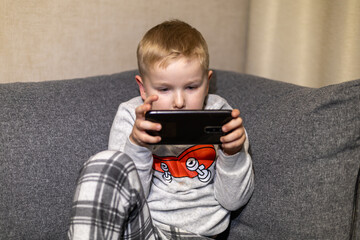 Child in pajamas engaged with smartphone while sitting on a couch at home during evening hours