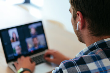 A freelancer sitting at a table in a modern living room, with headphones using a laptop for business video chat, conversation with friends and entertainment