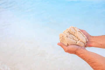 A person is holding a handful of sand on a beach