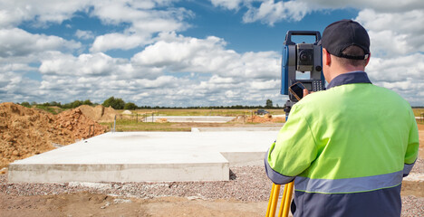 Surveyor with high-visibility clothing uses a total station to measure land at a construction site....