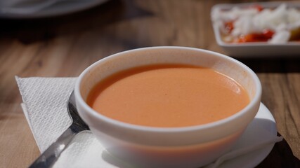Gazpacho bowl with spoon on napkin, accompanied by a tapa