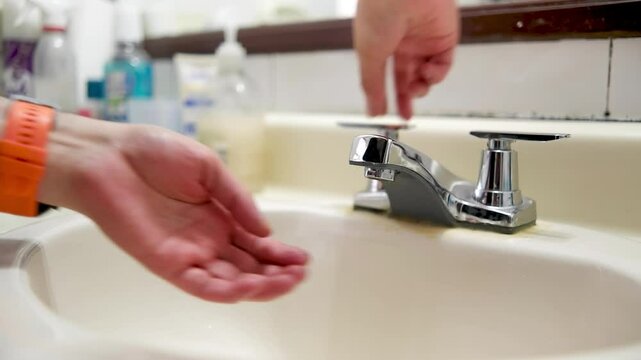 Two hands are going to wash their hands using the metal faucet in the bathroom sink, water service suspended, a topic of savings and hygiene