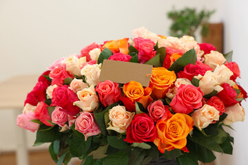 Bouquet of beautiful roses with blank card indoors, closeup