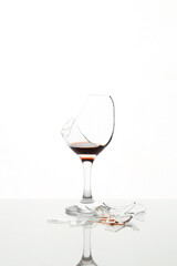 Pieces of broken glass with wine on table against white background