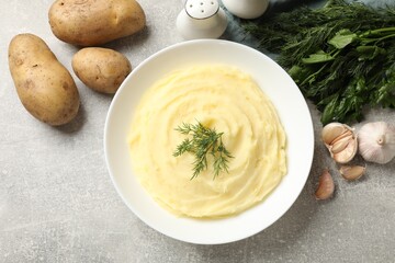 Tasty mashed potato in bowl, spices, herbs and raw vegetables on grey textured table, flat lay