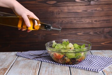 Woman pouring oil onto tasty salad at color wooden table, closeup