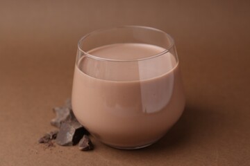 Tasty chocolate milk in glass and pieces of chocolate on brown background, closeup