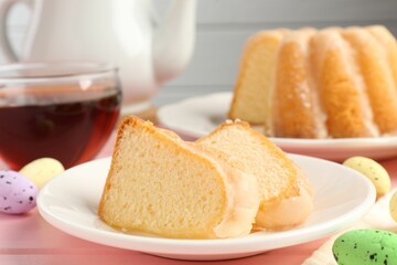Pieces of delicious bundt cake, Easter eggs and tea on pink wooden table, closeup