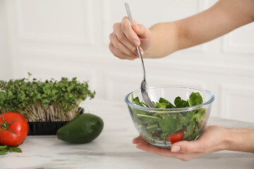 Woman in fitness clothes with salad at white marble table indoors, closeup. Healthy food