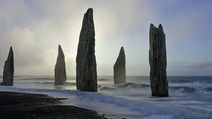 Dramatic rock formations on dark sand beach with ocean waves creating sea stacks in misty weather at the coast - Powered by Adobe