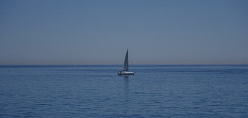 Obraz premium Sailboat sailing in a calm blue sea under a clear sky