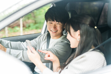 車内でスマホを見ながら会話する若いアジア人カップル,夫婦
