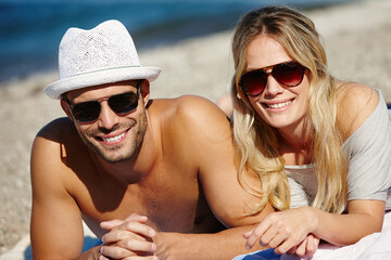 Couple, sunglasses and relax on beach towel, smile and peace on vacation or lying by water. People, happy and tropical ocean for bonding on weekend, outdoor nature and love for marriage or romance