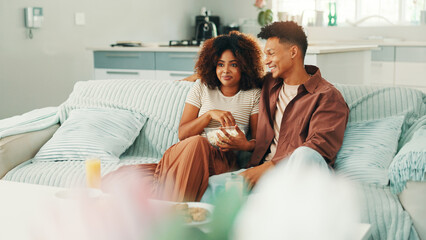 Obraz premium Couple, watching tv and popcorn at home with movies, series and affection. Man, woman and living room sofa for bonding, streaming online or snacks with subscription package for entertainment in house