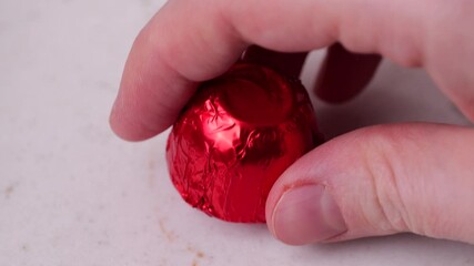 Fingers picking red chocolate candy on white marble table in slow motion