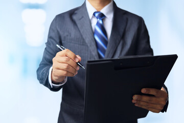 Businessman standing with a black file folder and holding a pen to sign or make an agreement on the document.
