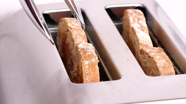 Metal tongs taking two toasted slices of bread out of a toaster on a white background, slow motion