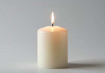 A solitary white pillar candle burning brightly against a plain light gray background in a studio setting