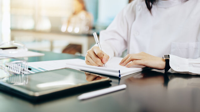 Woman, hands and writing with notebook for research, study or medical discovery at laboratory. Closeup, female person or scientist taking notes in exam, test or clinic trial for lab results on desk