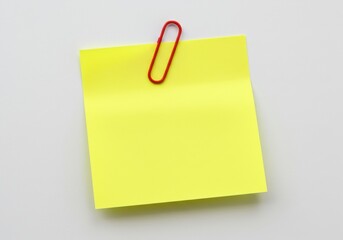 A yellow sticky note attached to a white surface with a red paper clip holding it in place