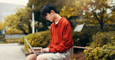 Asian man, student and laptop in park with typing, planning and creative writing for travel blog in...