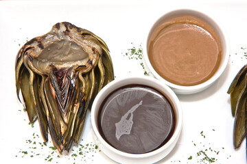 Grilled artichokes, grilled artichoke halves with sauces on a wooden table