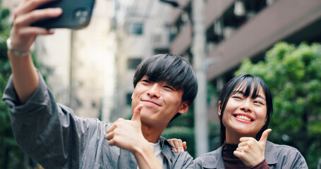 Happy, asian couple and city with thumbs up for selfie, photography or memory together in street. Japanese, man and woman with yes sign or like emoji for moment or picture in an urban town in Tokyo