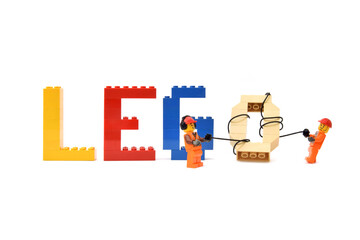 Naklejka premium Lego minifigures of workers in uniform are making a word lego from letters are made from bricks. Editorial illustrative image of popular plastic toy constructor.