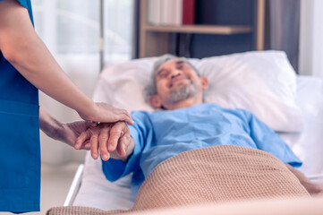 Fototapeta premium scene of elderly male patient looking at a nurse in uniform who supporting,holding hand and encourage him,focus at hands