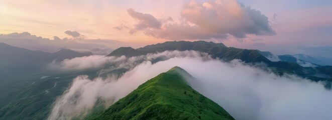 A panoramic view of lush green mountains enveloped in mist during sunset.