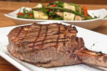 Grilled Tomahawk beef steak with green salad and asparagus, on a wooden table, food