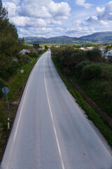 Scenic view of an empty asphalt country road winding through a green valley, under a cloudy sky