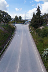 Scenic view of an empty two-lane road stretching towards a roundabout, framed by trees and under a cloudy sky