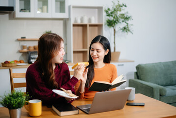 Two young Asian women brainstorming over coffee with a laptop and notebook at home.
