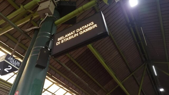 LED Display Showing "SEI DI S" Mounted on a Green Pole at a Train Station
