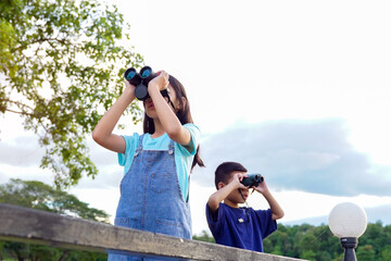 Children use binoculars to look at nature, birds, animals in the national park during family camping on vacation. with the concept of learning outside the classroom nature study, exploration.
